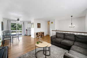 Living room with wood-type flooring and ceiling fan with notable chandelier