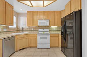 Kitchen featuring backsplash, tile counters, sink, and white appliances