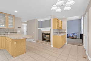 Kitchen featuring a tile fireplace, tile countertops, tasteful backsplash, light brown cabinetry, and light colored carpet