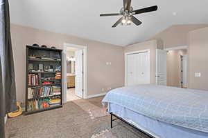 Carpeted bedroom featuring ensuite bath, ceiling fan, a closet, and lofted ceiling