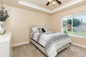 Bedroom with ceiling fan, a tray ceiling, crown molding, and light carpet