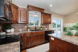 Kitchen with light hardwood / wood-style floors, tasteful backsplash, black appliances, hanging light fixtures, and sink