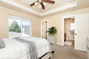 Carpeted bedroom featuring a tray ceiling, ceiling fan, ensuite bath, and access to exterior