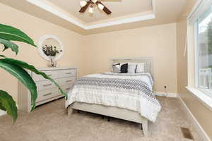 Carpeted bedroom with a tray ceiling, ornamental molding, and ceiling fan