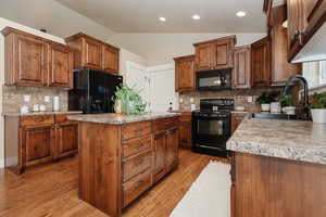 Kitchen with backsplash, black appliances, light wood-type flooring, sink, and lofted ceiling