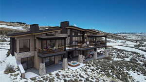 Snow covered property featuring stone siding, a chimney, and a patio