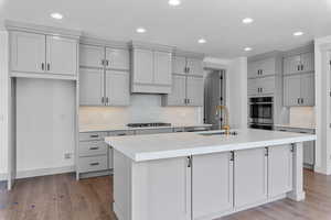 Kitchen with light hardwood / wood-style floors, sink, tasteful backsplash, and an island with sink