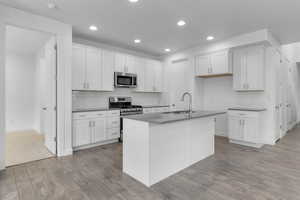 Kitchen with stainless steel appliances, sink, a center island with sink, white cabinets, and light hardwood / wood-style floors