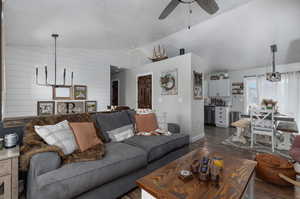 Living room featuring dark wood-type flooring, wooden walls, ceiling fan with notable chandelier, and lofted ceiling