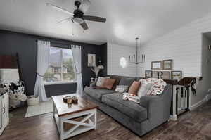 Living room featuring wooden walls, ceiling fan with notable chandelier, lofted ceiling, and dark wood-type flooring