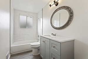 Full bathroom with tiled shower / bath combo, hardwood / wood-style floors, toilet, and vanity