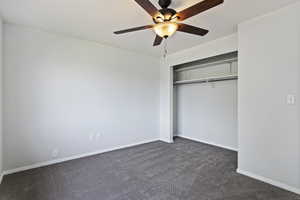 Unfurnished bedroom featuring a closet, dark colored carpet, and ceiling fan