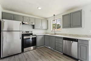 Kitchen featuring appliances with stainless steel finishes, hardwood / wood-style flooring, gray cabinets, and hanging light fixtures