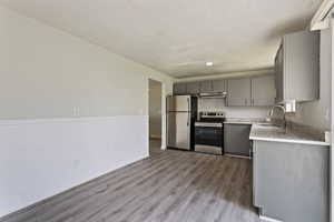 Kitchen with light stone counters, stainless steel appliances, hardwood / wood-style flooring, gray cabinets, and sink