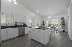 Kitchen with stainless steel dishwasher, lofted ceiling, white cabinetry, and dark hardwood / wood-style floors