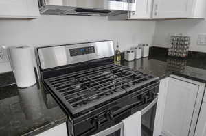 Kitchen with dark stone countertops, white cabinets, and stainless steel gas stove