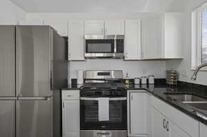 Kitchen with appliances with stainless steel finishes, dark stone countertops, white cabinetry, and sink