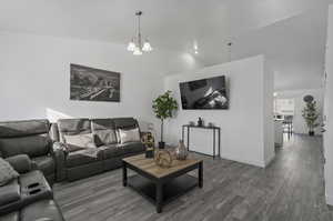 Living room with dark hardwood / wood-style floors, lofted ceiling, and an inviting chandelier