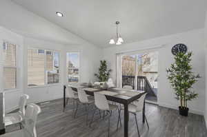 Dining room with dark wood-type flooring, a notable chandelier, and vaulted ceiling