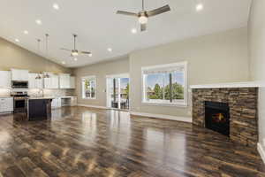 Unfurnished living room with a stone fireplace, ceiling fan, and dark wood-type flooring