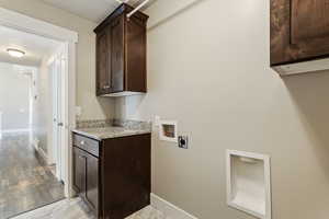 Clothes washing area with cabinets, hookup for an electric dryer, washer hookup, and light hardwood / wood-style flooring