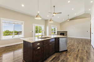 Kitchen with a fireplace, a center island with sink, dark hardwood / wood-style flooring, dishwasher, and ceiling fan