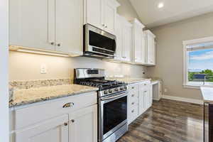 Kitchen featuring white cabinetry, dark wood-type flooring, lofted ceiling, appliances with stainless steel finishes, and light stone counters