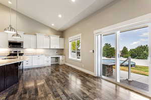 Kitchen with dark hardwood / wood-style floors, high vaulted ceiling, sink, white cabinets, and appliances with stainless steel finishes