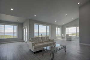 Living room with plenty of natural light, a lake view, wood-type flooring, and vaulted ceiling