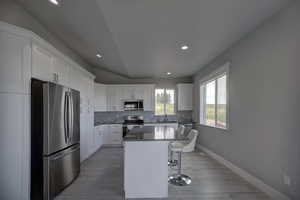 Kitchen with stainless steel appliances, white cabinetry, a center island, and wood-type flooring