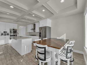 Kitchen with a sink, wall chimney exhaust hood, stainless steel appliances, backsplash, and coffered ceiling
