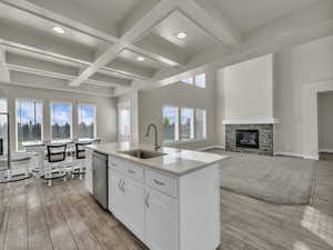 Kitchen with stainless steel dishwasher, a center island with sink, a sink, coffered ceiling, and white cabinetry