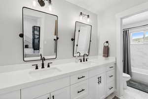 Full bathroom featuring dual bowl vanity, toilet, tile floors, and shower / tub combo with curtain