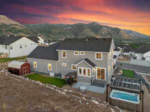 Back house at dusk with a patio area, a mountain view, a hot tub, central air condition unit, and a shed