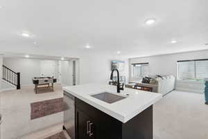 Kitchen with an island with sink, sink, dishwasher, and light carpet