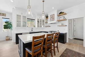 Kitchen featuring decorative light fixtures, light wood-type flooring, a kitchen island, sink, and white cabinets