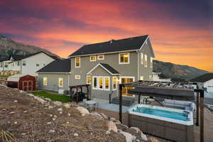 Back house at dusk featuring a pergola, a storage unit, a patio, a mountain view, and a hot tub