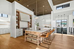 Kitchen with high end stove, a large island, a towering ceiling, and white cabinets