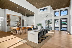 Kitchen with a high ceiling, a large island with sink, pendant lighting, a kitchen bar, and light wood-type flooring