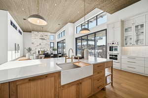 Kitchen with a high ceiling, sink, decorative light fixtures, white cabinetry, and wood ceiling