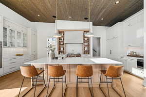 Kitchen with decorative backsplash, light hardwood / wood-style flooring, hanging light fixtures, and a large island