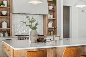 Kitchen with pendant lighting, decorative backsplash, a kitchen breakfast bar, and range hood