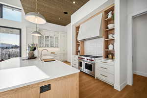 Kitchen with custom exhaust hood, range with two ovens, sink, hanging light fixtures, and light hardwood / wood-style flooring