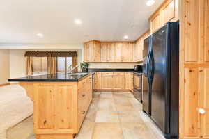 Kitchen featuring light brown cabinetry, black fridge, a kitchen breakfast bar, range with electric cooktop, and sink