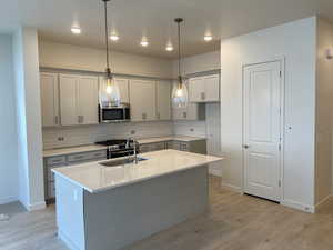 Kitchen featuring hanging light fixtures, stainless steel appliances, backsplash, a center island with sink, and light hardwood / wood-style floors