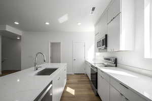 Kitchen featuring stainless steel appliances, sink, hardwood / wood-style flooring, and light stone counters