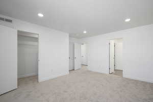 Unfurnished bedroom with a walk in closet, a closet, and light colored carpet