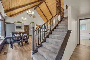 Stairs featuring light hardwood / wood-style floors, an inviting chandelier, beamed ceiling, wooden ceiling, and high vaulted ceiling