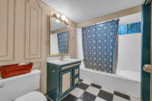 Full bathroom featuring tile flooring, a textured ceiling, shower / tub combo, vanity with extensive cabinet space, and toilet