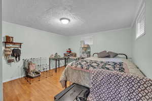 Bedroom with hardwood / wood-style flooring, a textured ceiling, and crown molding